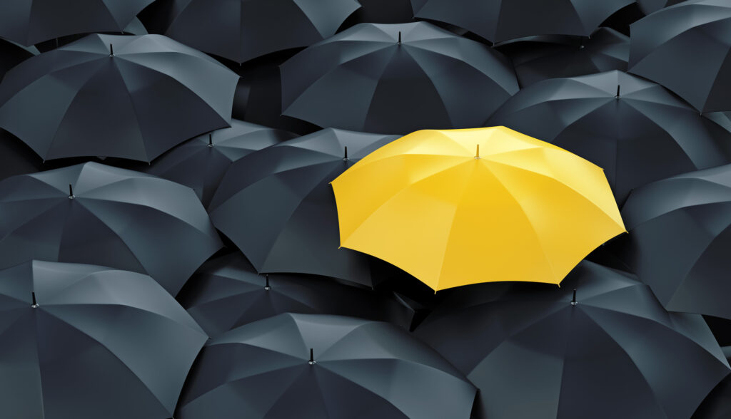 Yellow umbrella standing out in the mass of black umbrellas, depicting the risks of not having a general liability insurance for real estate agents.